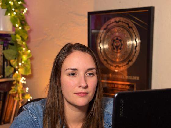 Malia at her desk, her Certified Funnel Builder award on the wall behind her