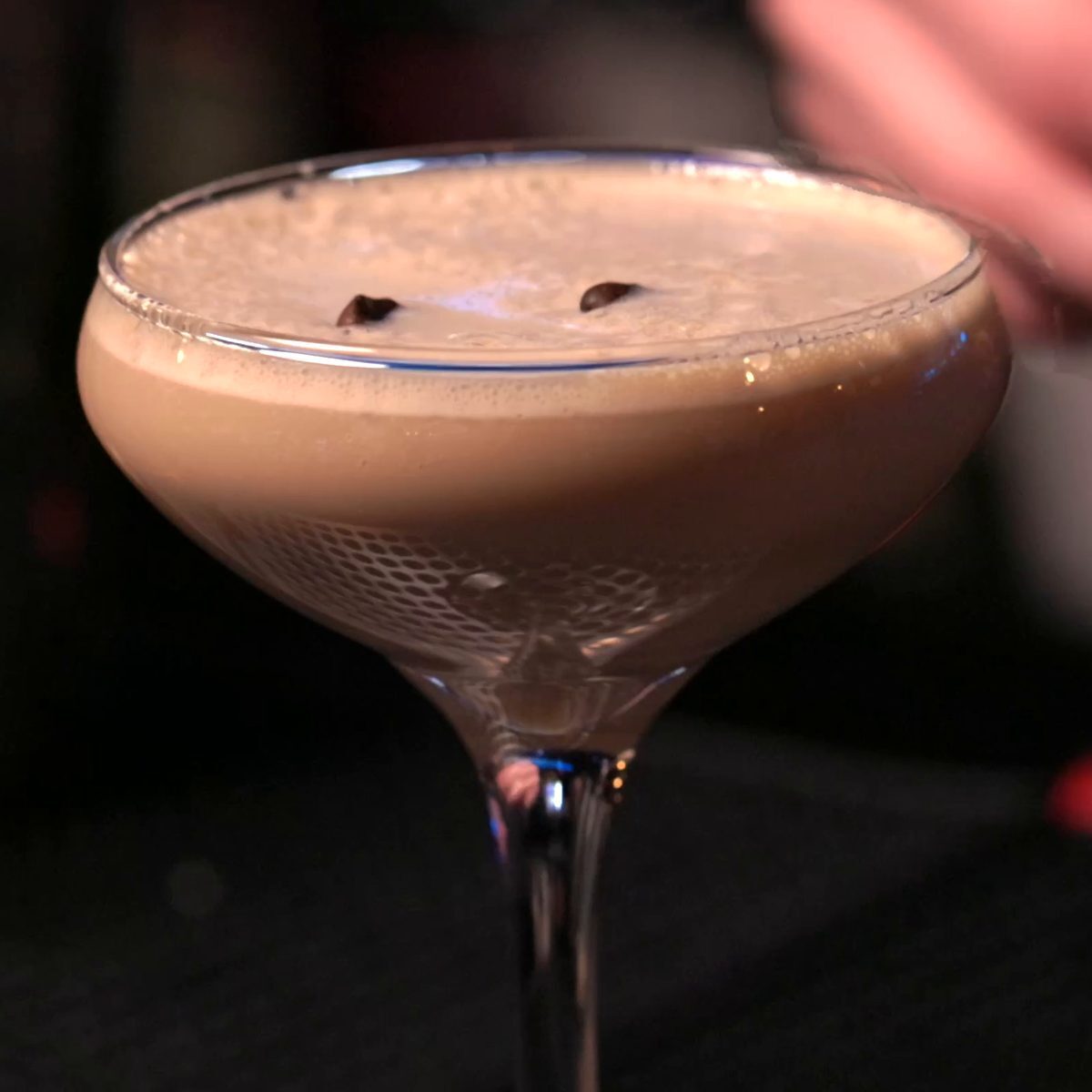 An espresso martini with a thick foam and coffee beans, served in a coupe on a bar