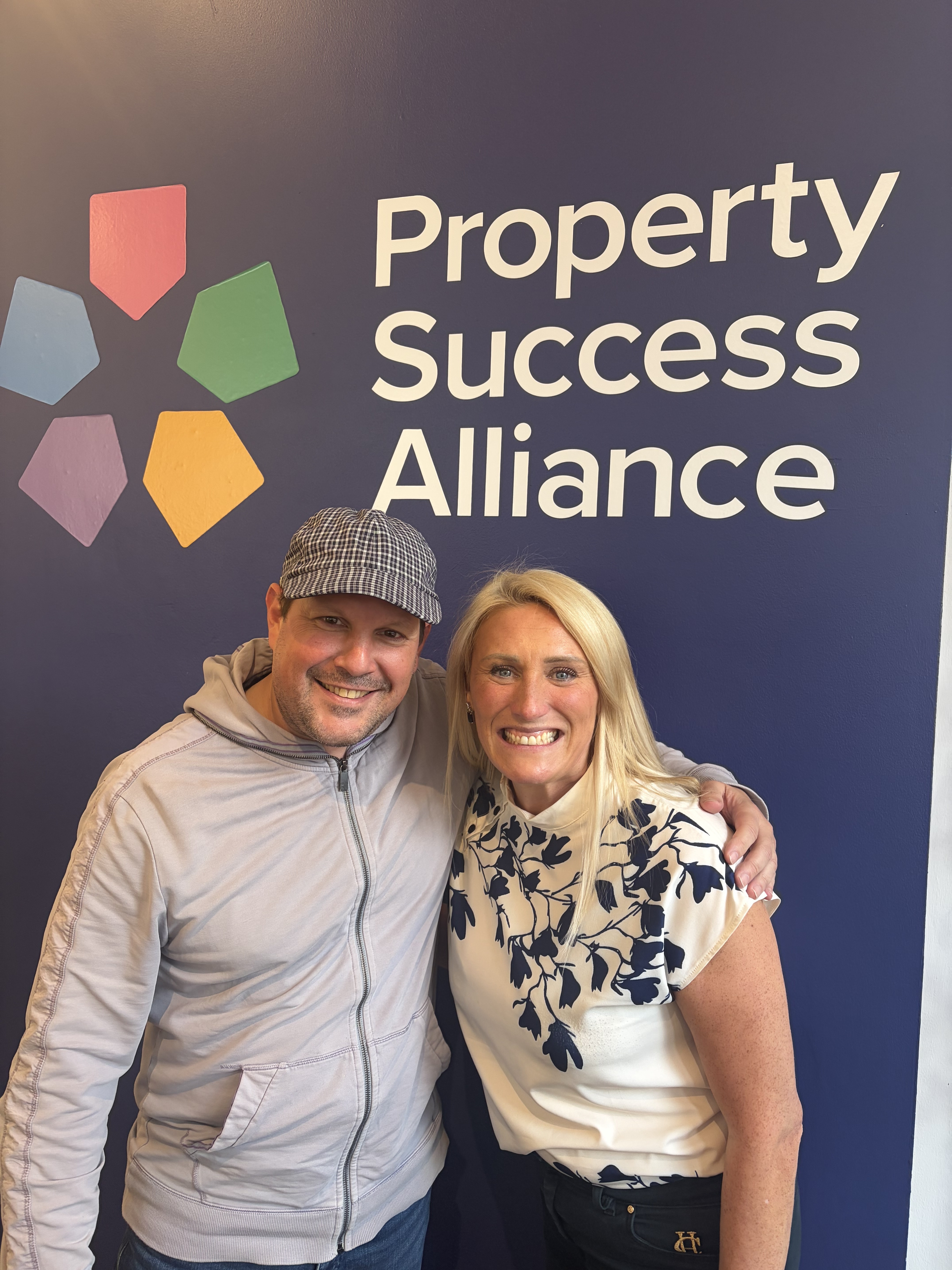 Katy with a community member in front of the Property Success Alliance wall