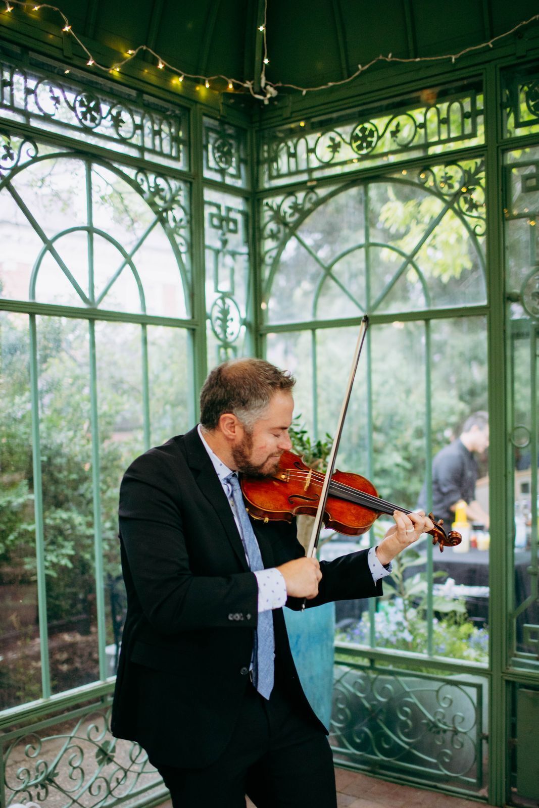 Violinist playing cocktail hour music inside a green glass garden conservatory
