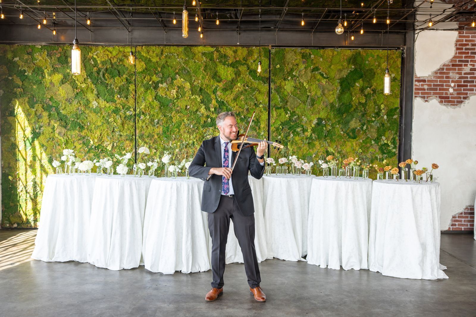 Electric violinist Jared Judge performing in front of a living moss wall and a long reception table
